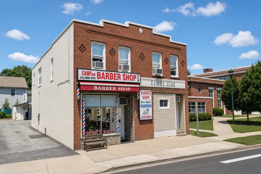 Camp Ave Barbershop storefront in Merrick, NY — red awning, two barber poles, brick corner building